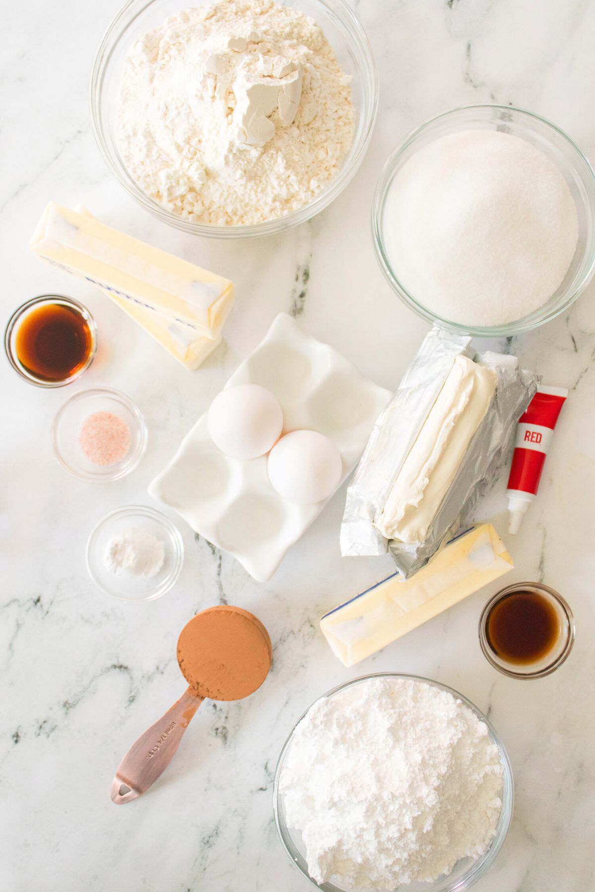 Ingredients needed to make red velvet bars measured in small dishes on a white marble table. 