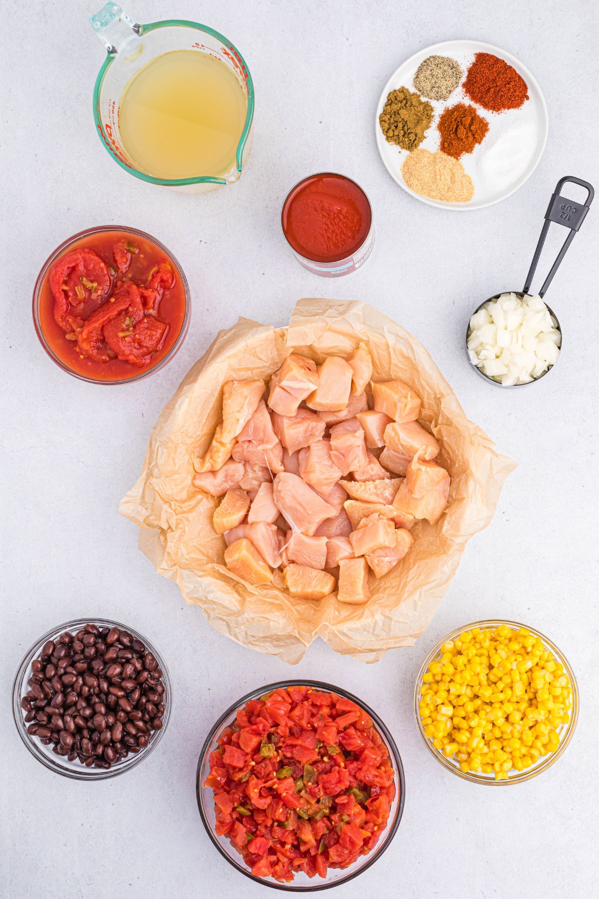 Ingredients needed to make chicken chili measured into small bowls on a white marble.