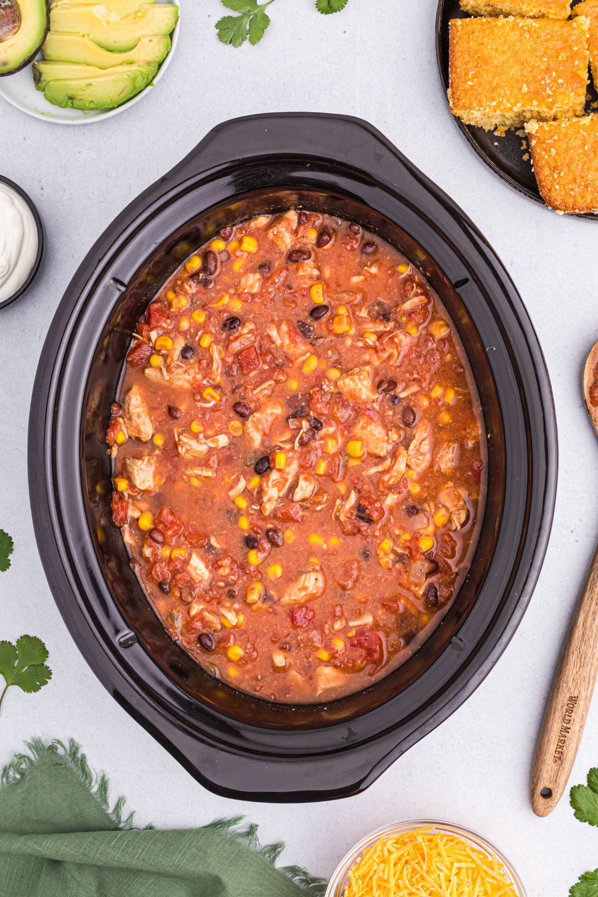 Chili cooked in the slow cooker with toppings and corn bread on the table. 