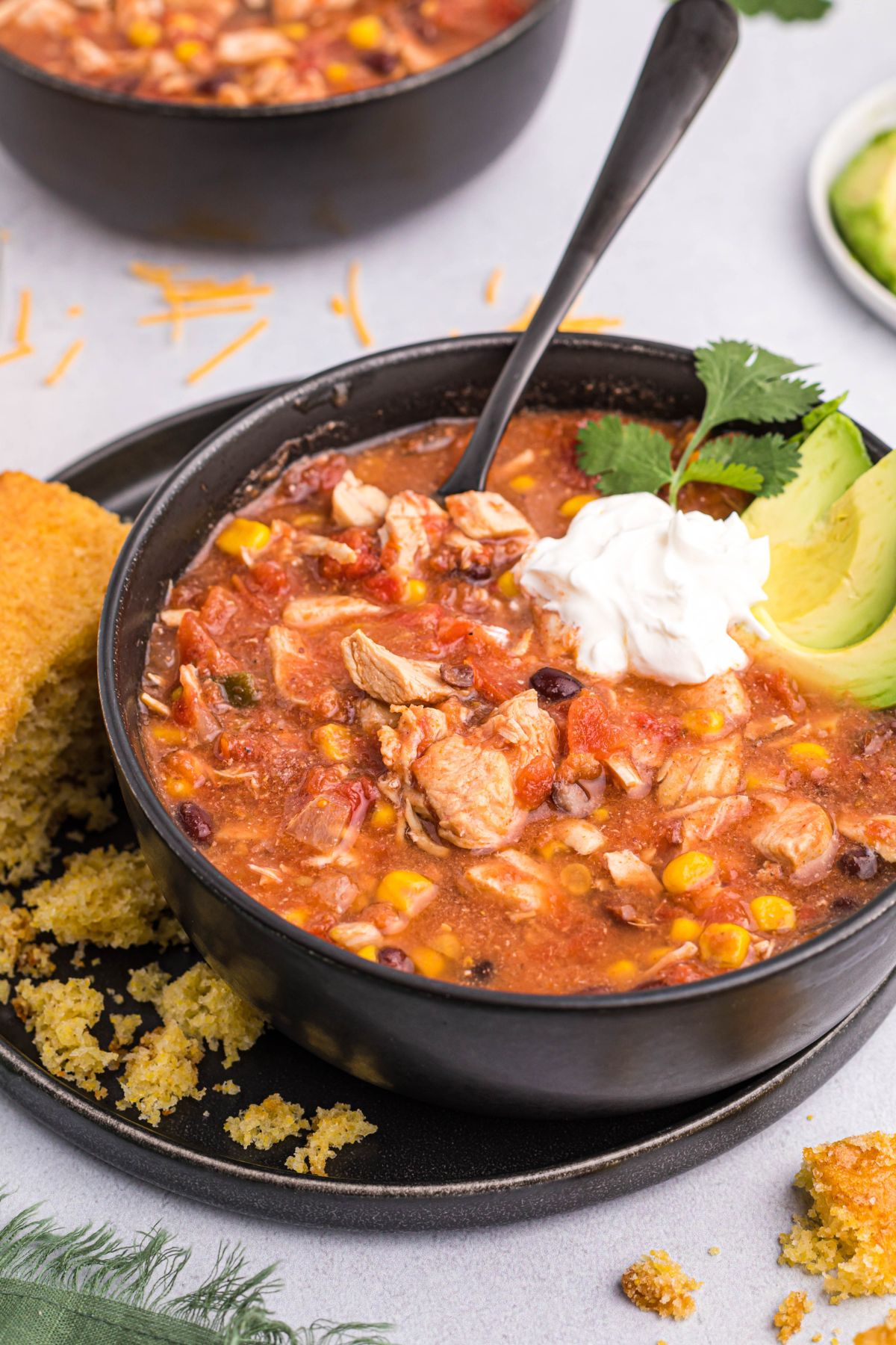 Chili served in a black bowl topped with sour cream and avocados. 