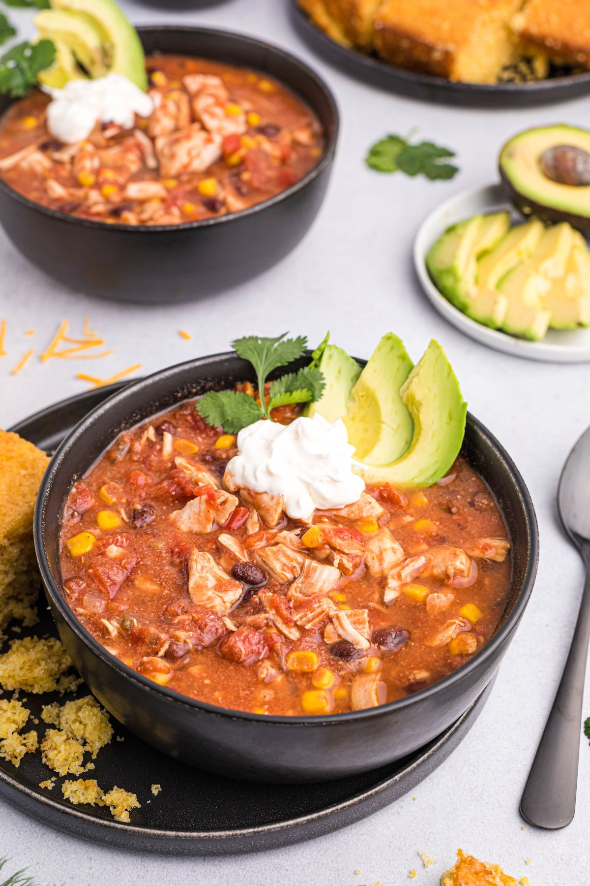 Slow cooker chicken chili in a black bowl topped with avocado slices and sour cream. 