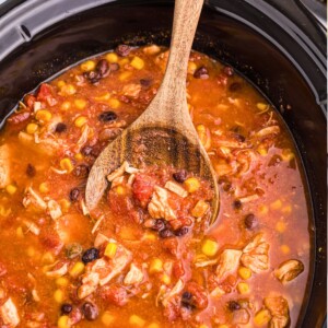 Chicken chili in a black slow cooker with a wooden spoon serving it.