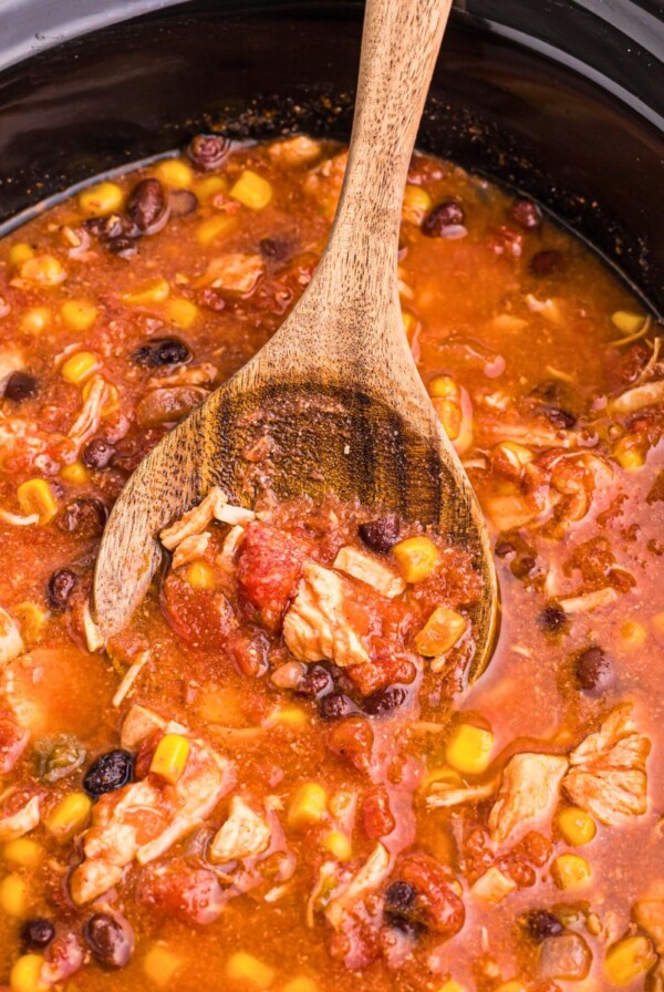 Chicken chili in a black slow cooker with a wooden spoon serving it.