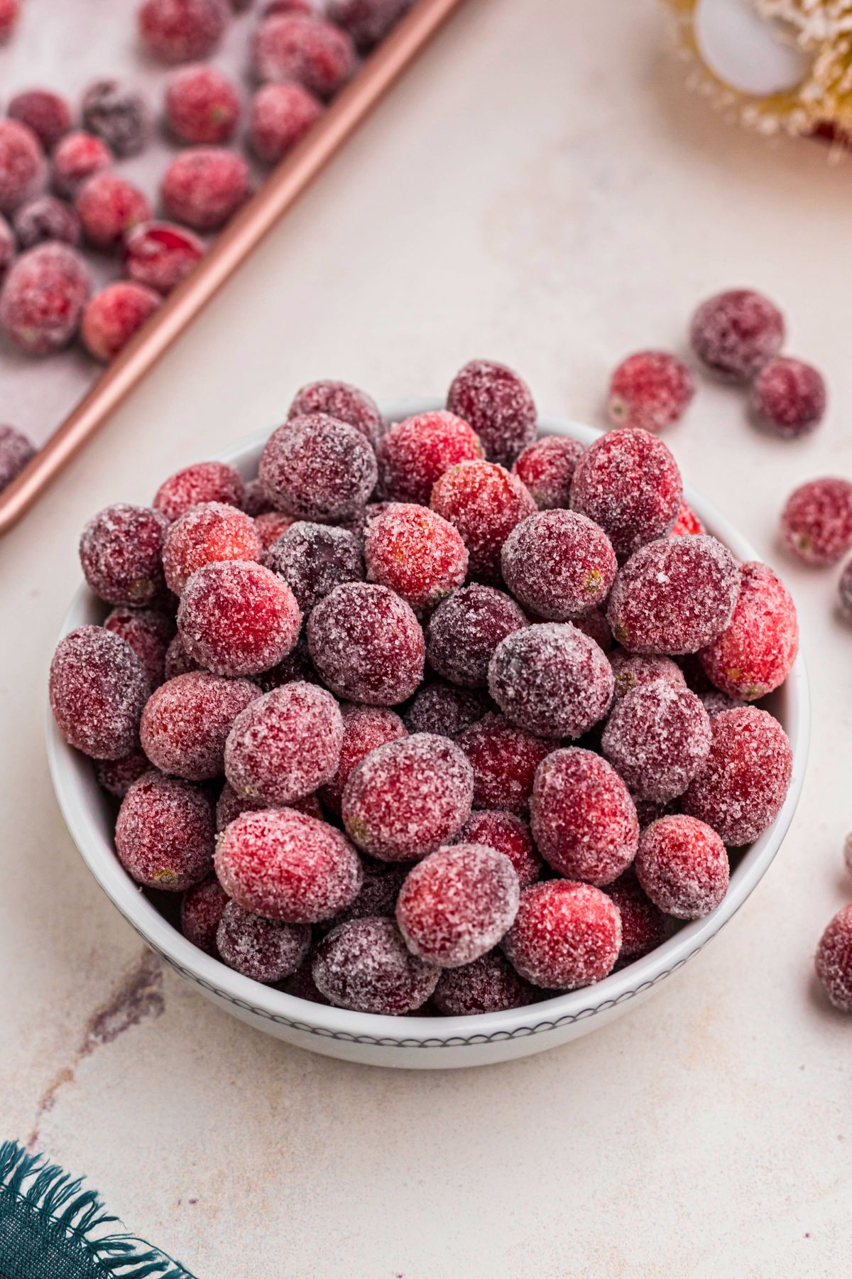 Sugared cranberries in a small white bowl on a marble table. 