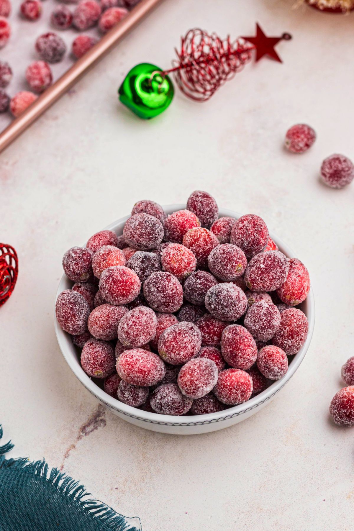 Red cranberries coated in sugar in a white bowl with holiday ornaments on the table 