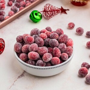 Sugared cranberries in a small white bowl on a marble table.