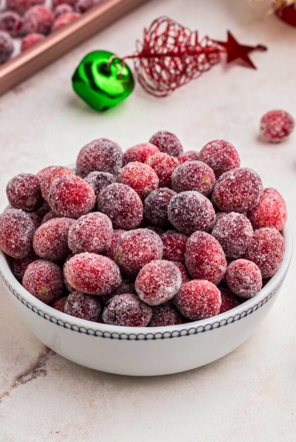 Sugared cranberries in a small white bowl on a marble table.