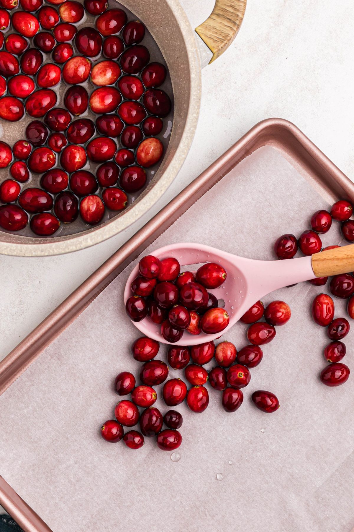 Syrup coated cranberries being scooped onto parchment paper lined baking sheet so they can dry at room temp. 