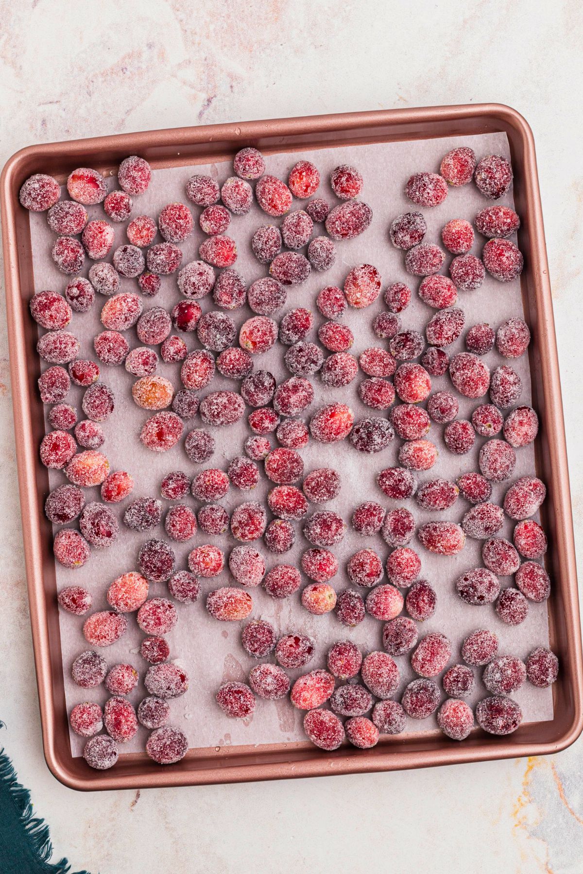 Sugared cranberries on a rose colored baking sheet. 