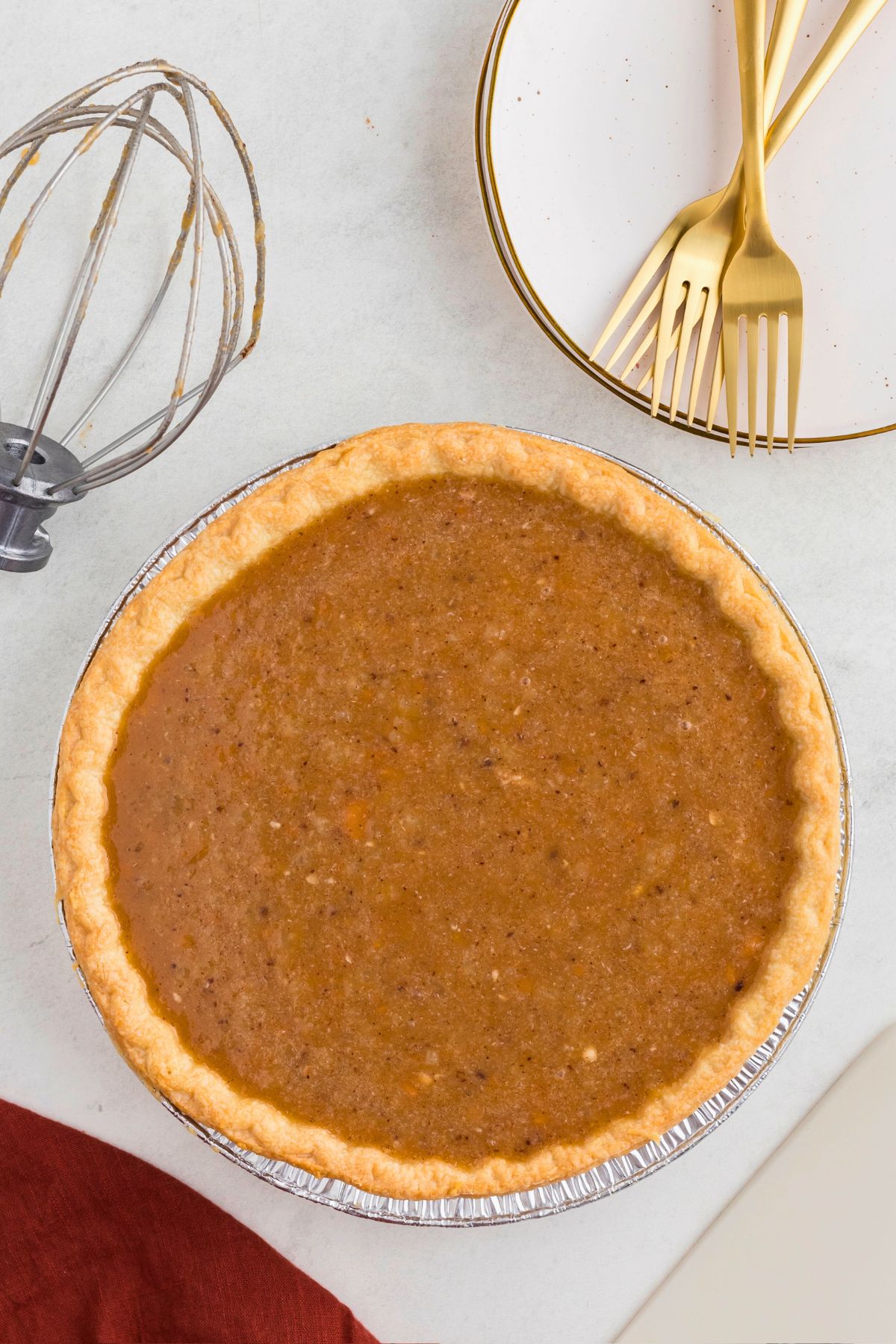 Uncooked sweet potato pie in a golden crust in front of small white plates. 