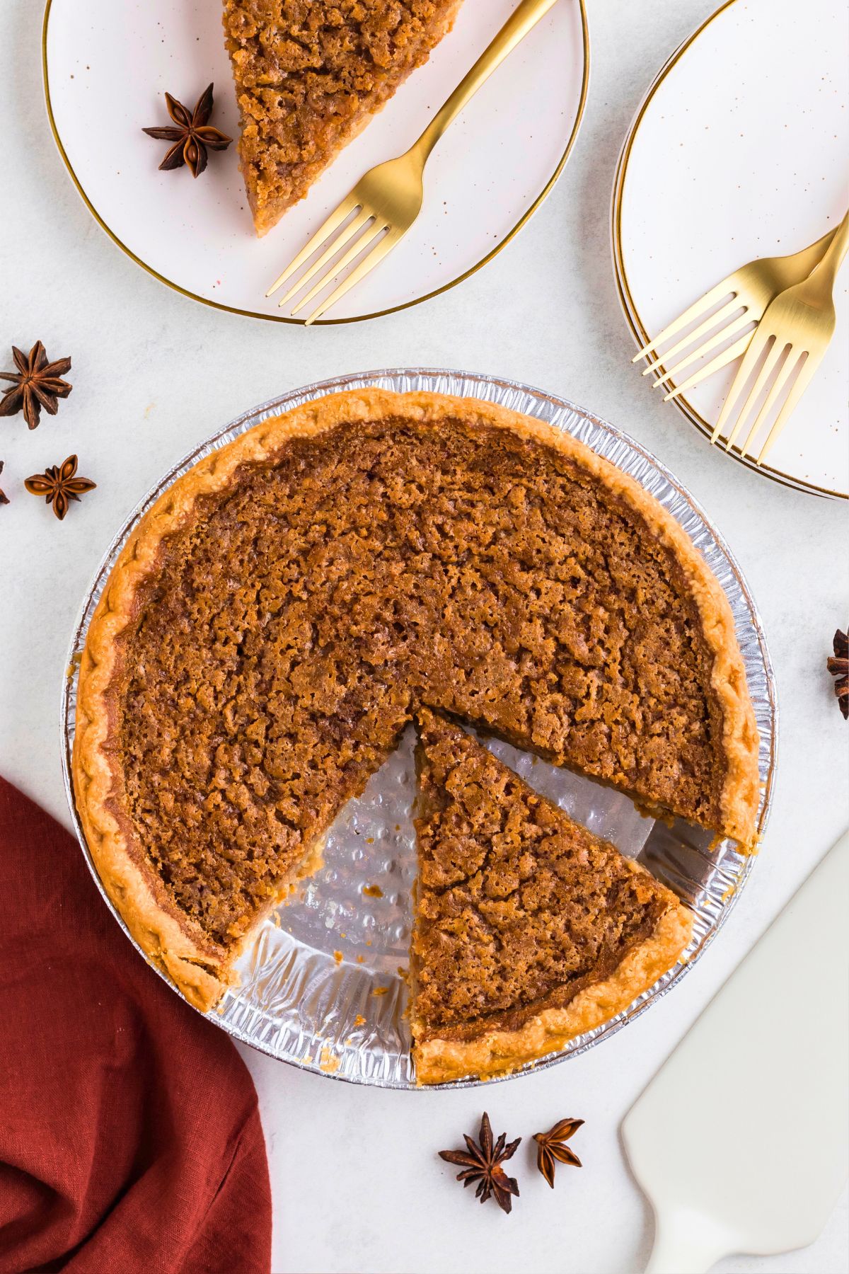 Golden brown sweet potato pie in a pie plate with a slice cut on a small white plate next to it. 