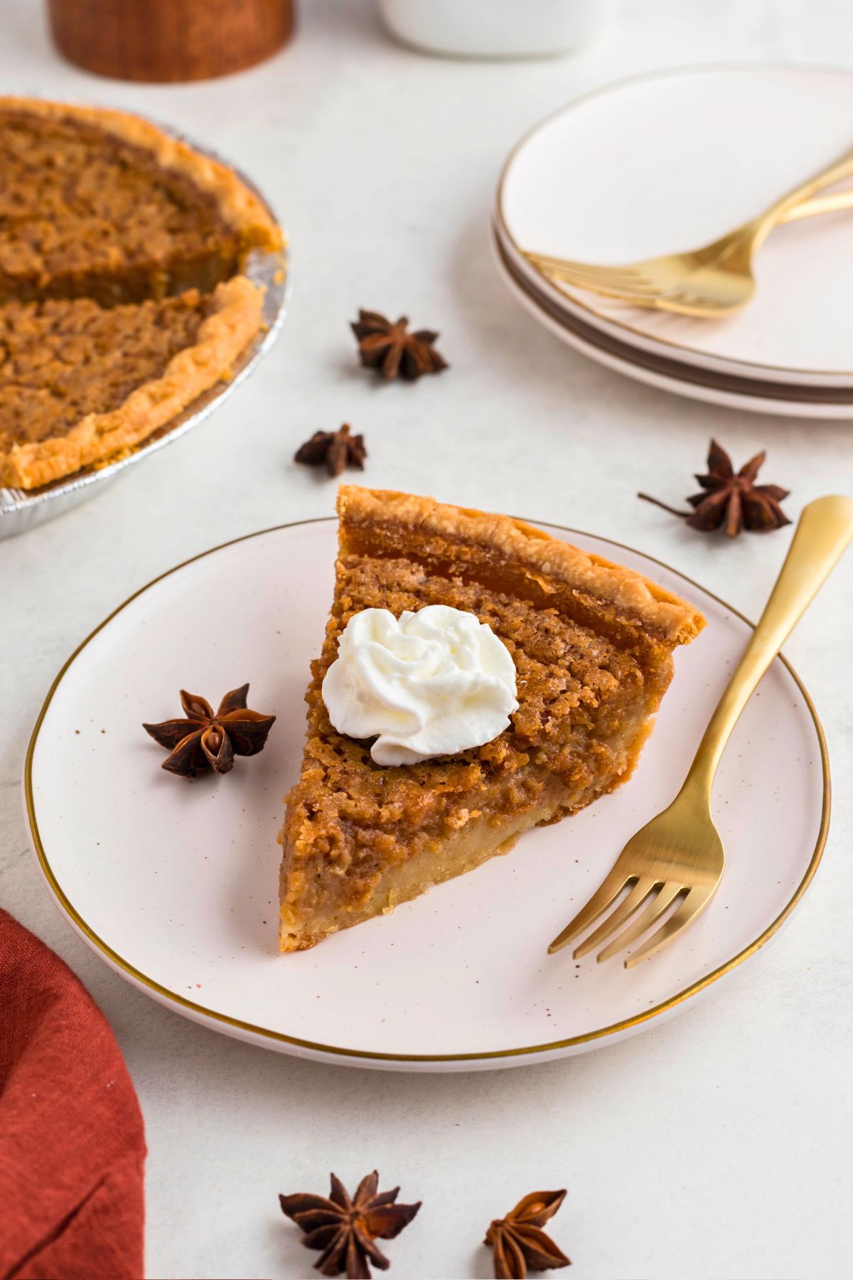 Slice of sweet potato pie, topped with whipping cream on a small white plate with a gold fork. 