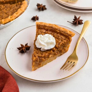 Golden slice of sweet potato pie on a small white plate with a gold fork.