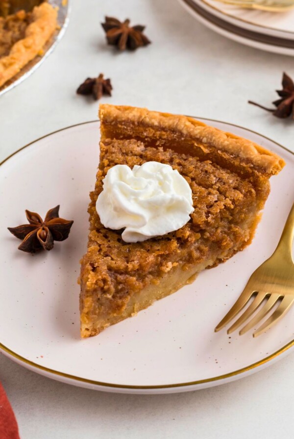 Golden slice of sweet potato pie on a small white plate with a gold fork.