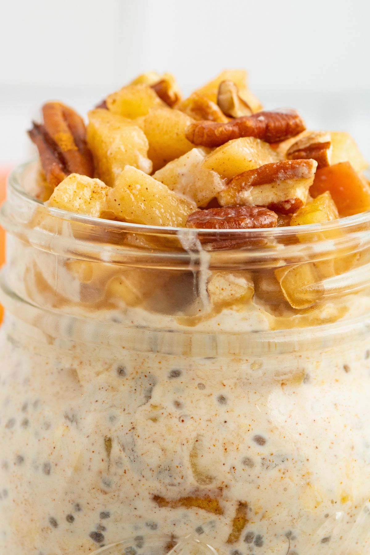 Close up photo of apple pie overnight oats in a mason jar, topped with crushed nuts and apples. 