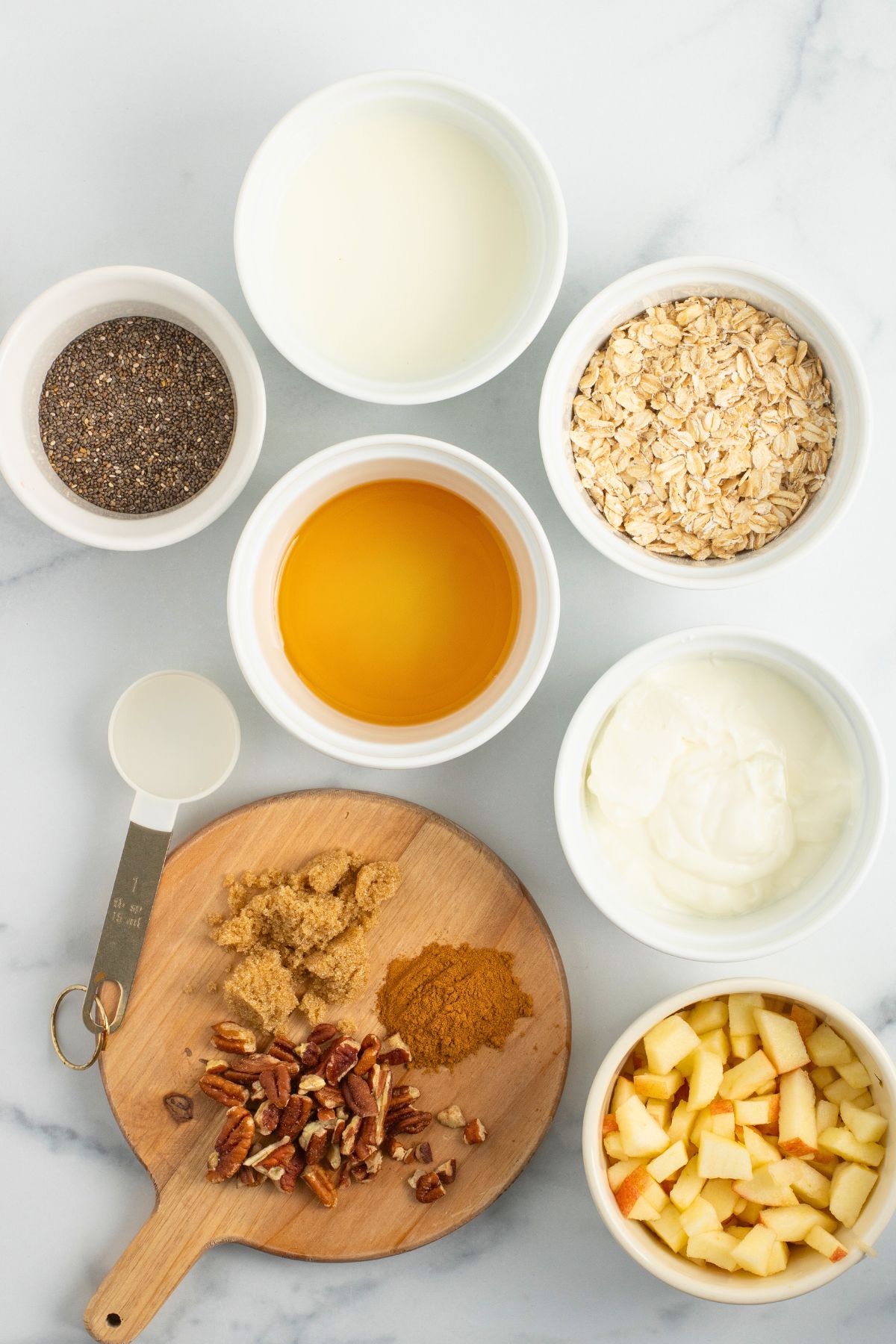 Ingredients needed to make overnight oats measured out in small bowls on a marble table. 