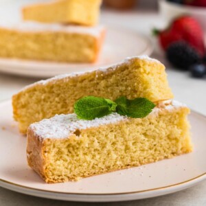 Golden yellow butter cake slices on white plates topped with powdered sugar with berries on the table.