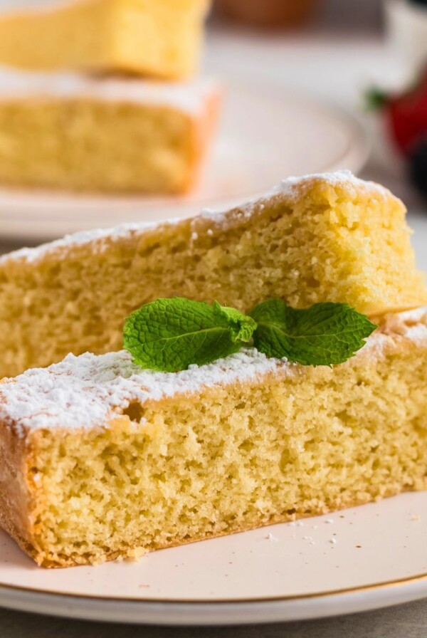 Golden yellow butter cake slices on white plates topped with powdered sugar with berries on the table.