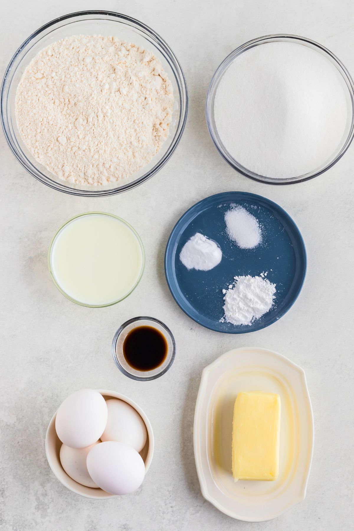 Ingredients needed to make butter cake measured out in glass bowls on a marble table. 