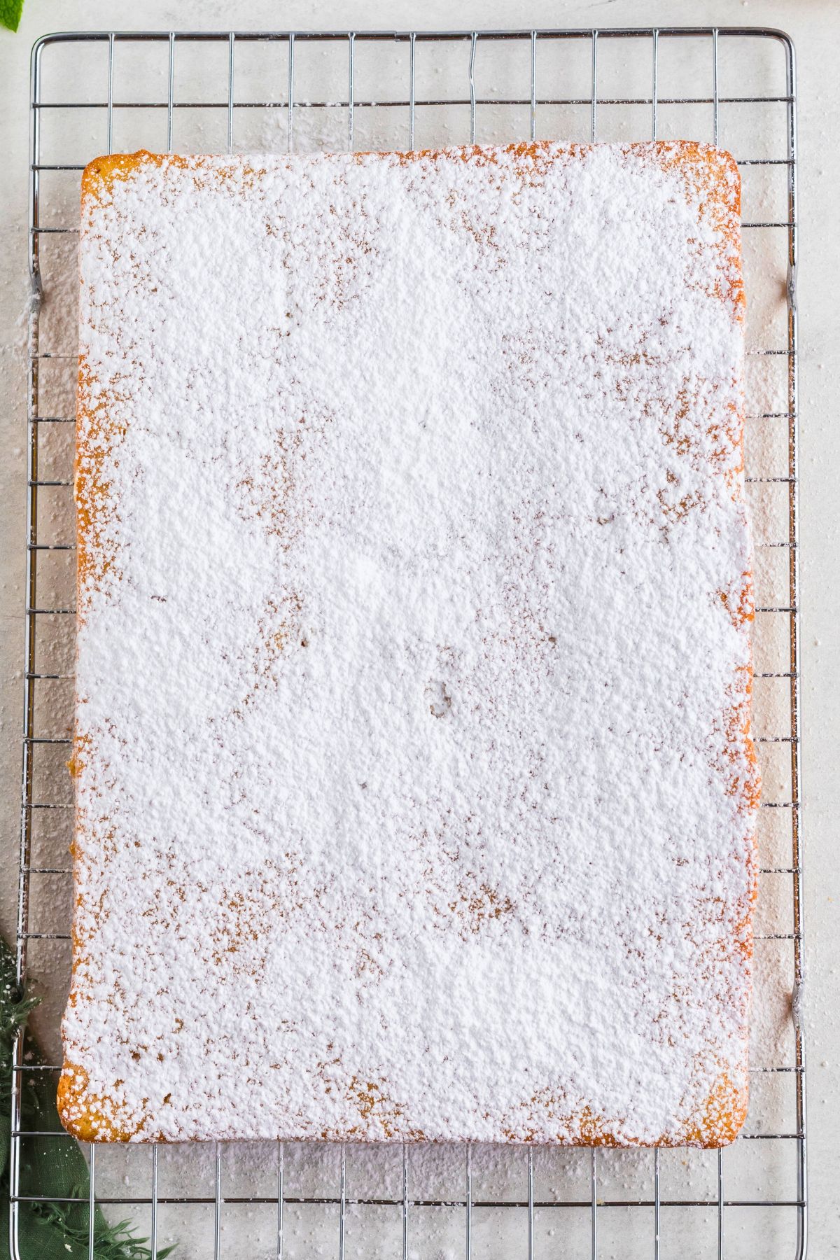 Baked golden butter cake on a wire cooling rack and covered with a light dusting of powdered sugar. 