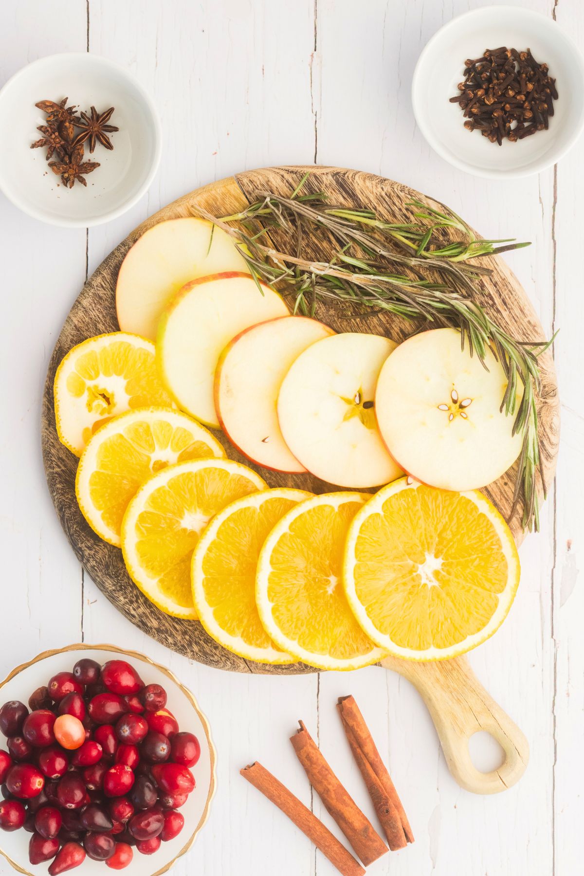 Fruit slices and spices measured on a cutting board on a white wood table. 