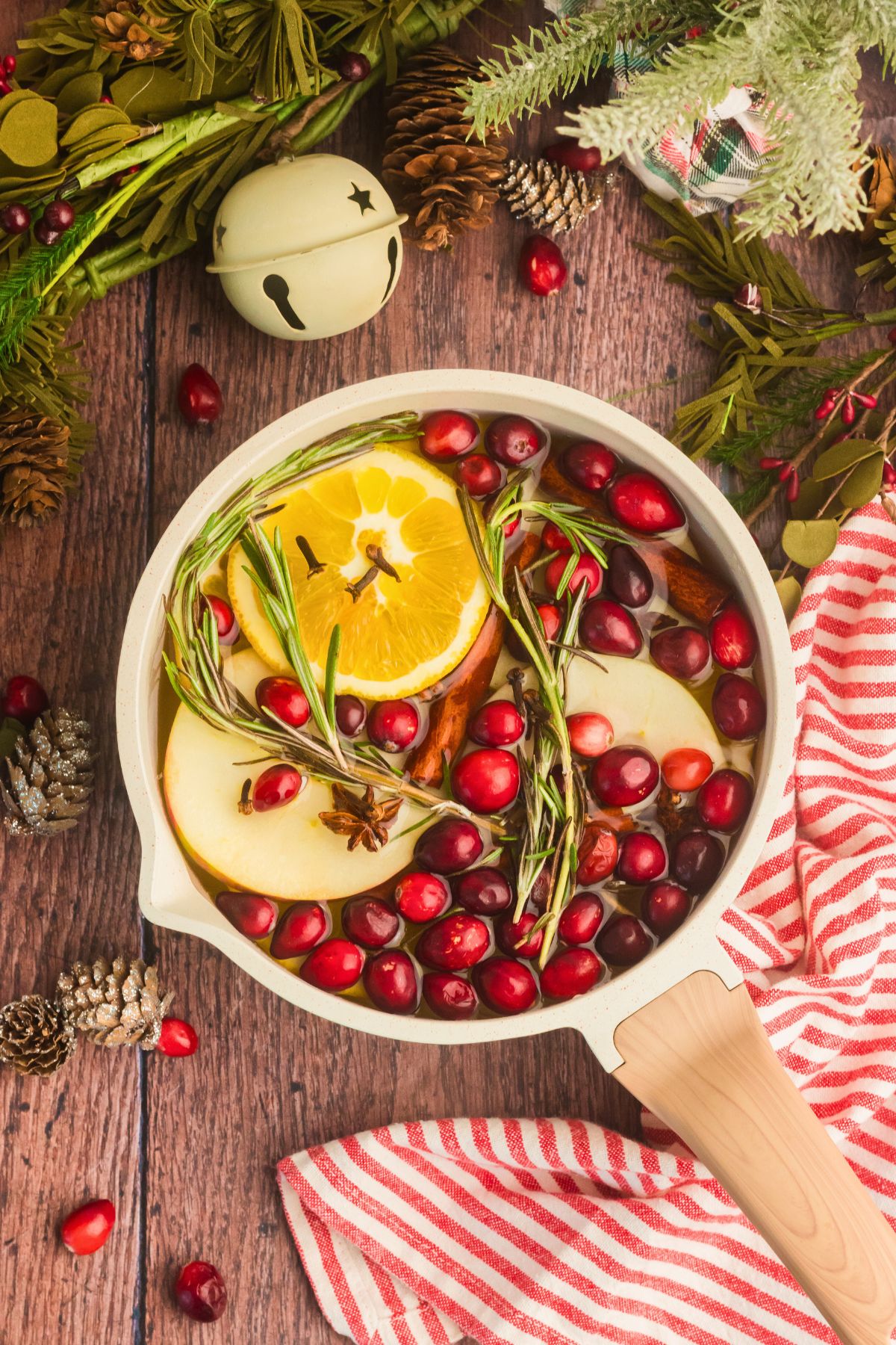 Cream colored saucepan filled with water, cranberries, fruit slices, and other ingredients to make a Christmas simmer pot.