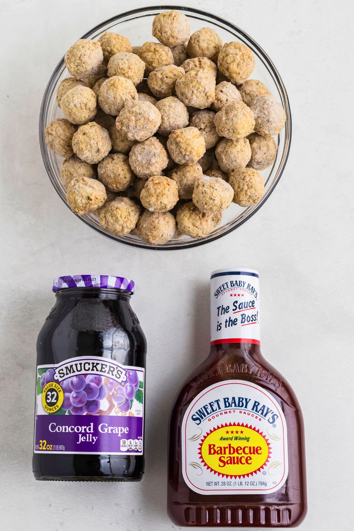 Frozen meatballs, grape jelly, and BBQ sauce, on a white marble table before mixing together in a crock pot and cooking. 