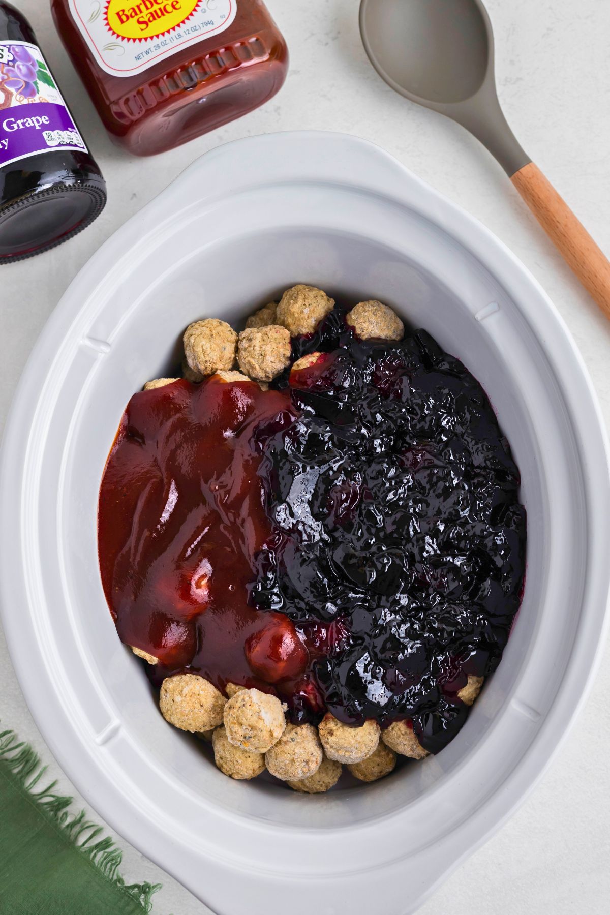 Frozen meatballs, grape jelly, and bbq sauce in a white slow cooker before cooking. 