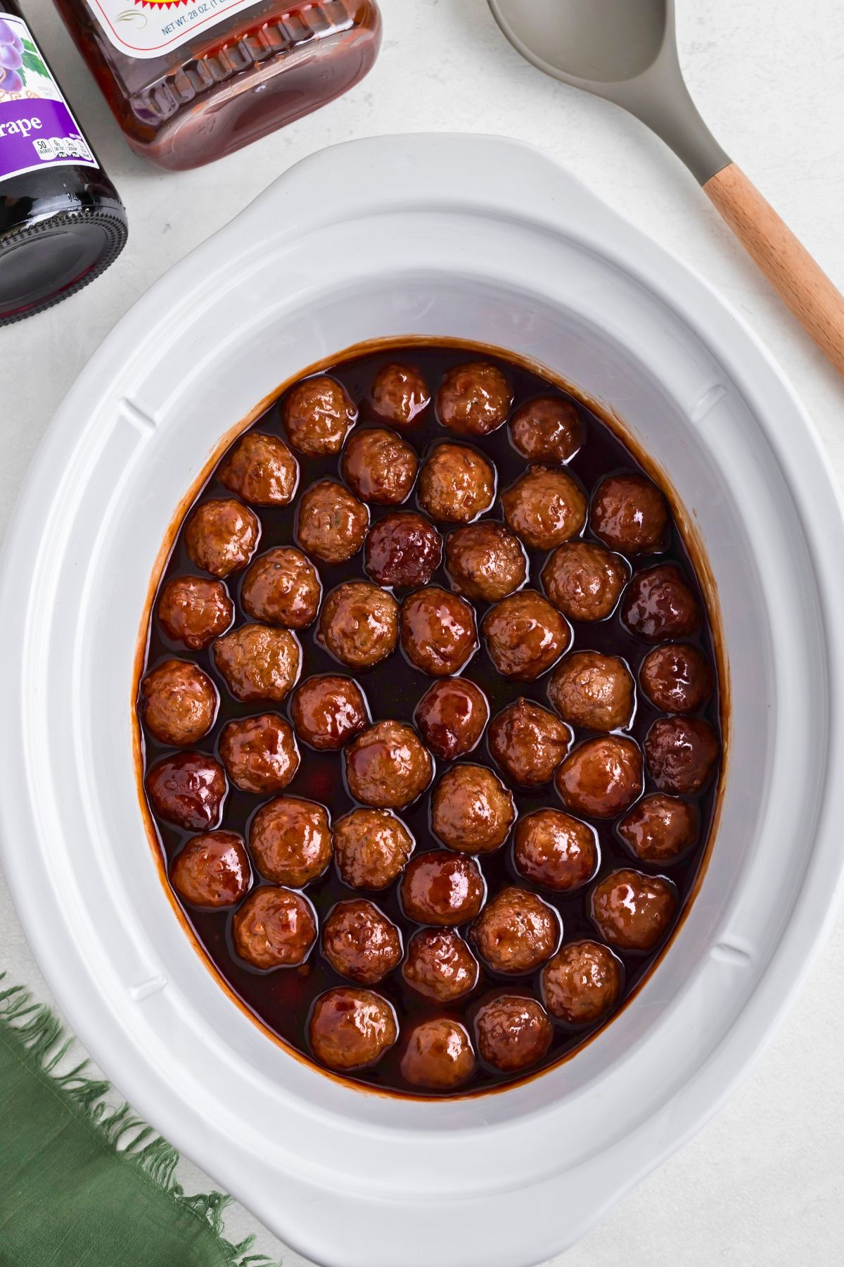 Grape jelly meatballs in a white slow cooker after cooking for 3-4 hours. 