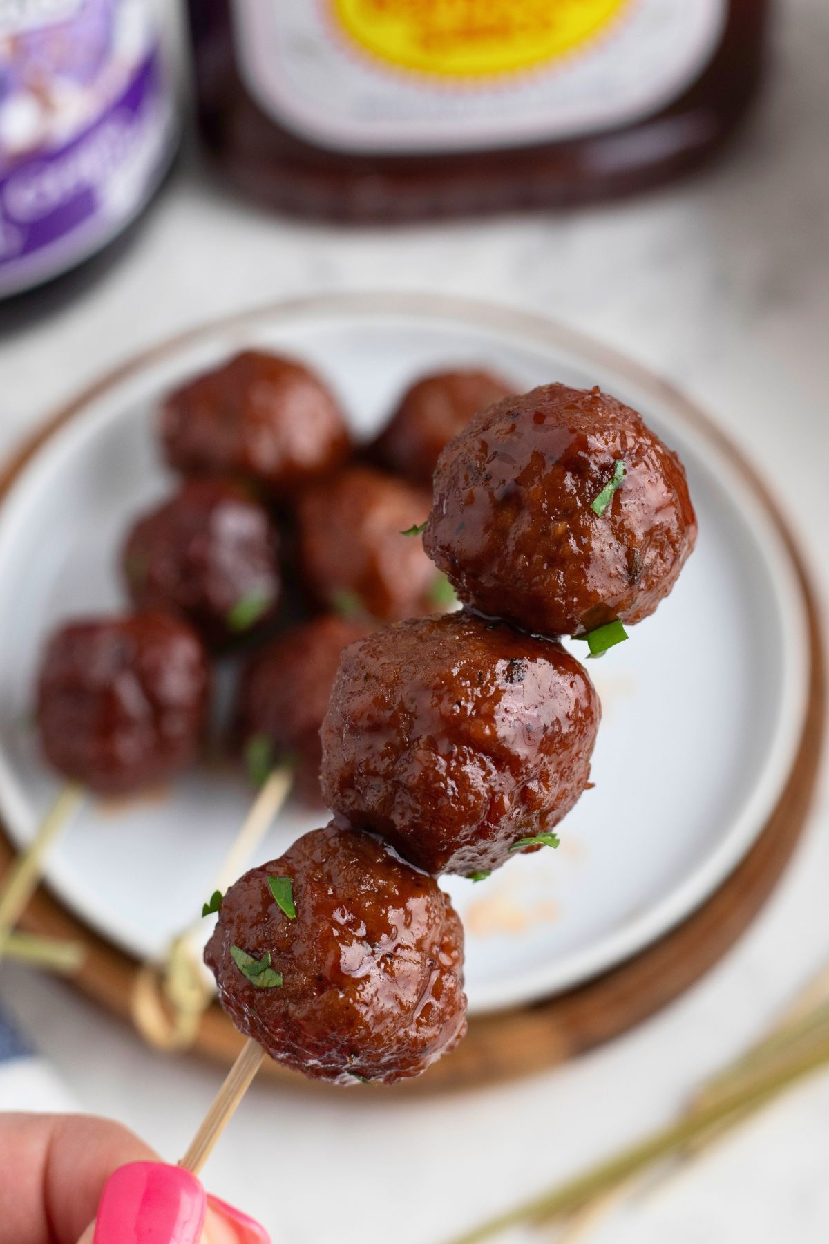 Three meatballs on a skewer over a small white appetizer plate. 