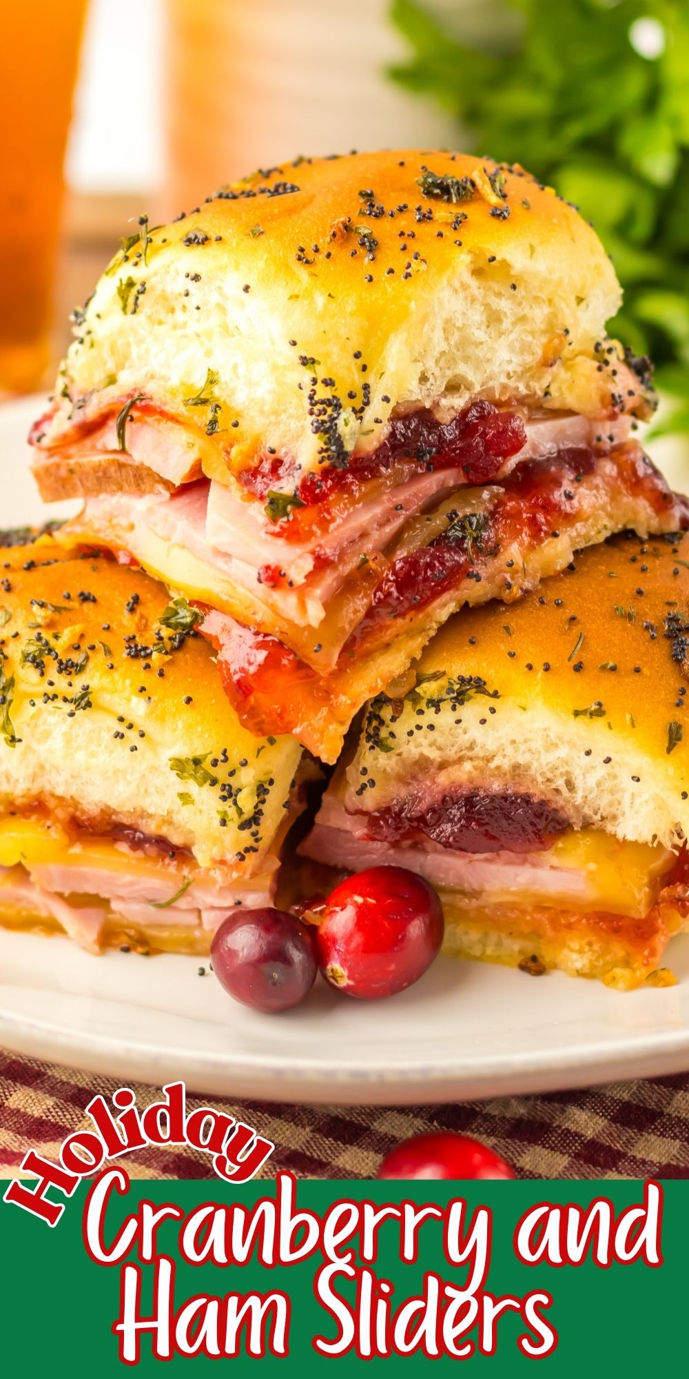 Cranberry and ham sliders stacked on a white plate with red cranberries as a garnish.