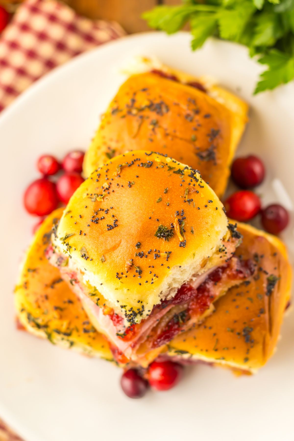 Cranberry and ham sliders stacked on a white plate with red cranberries as a garnish.