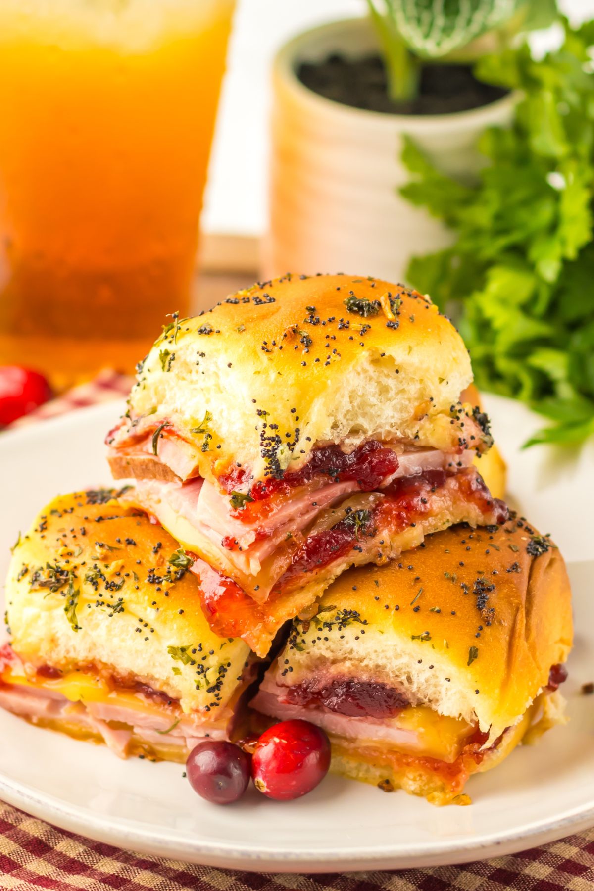 Cranberry and ham sliders stacked on a white plate with red cranberries as a garnish.