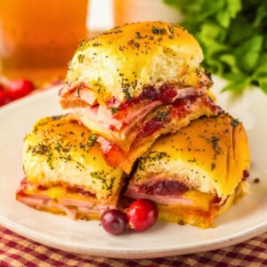 Cranberry and ham sliders stacked on a white plate with red cranberries as a garnish.