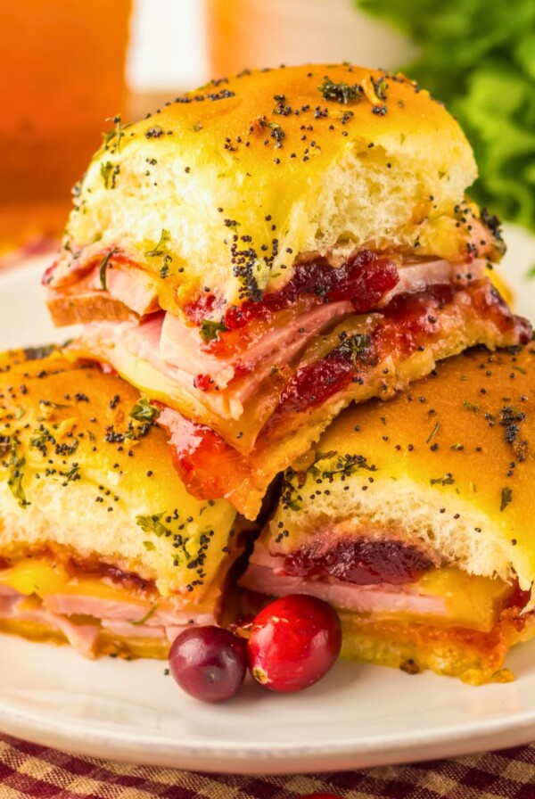 Cranberry and ham sliders stacked on a white plate with red cranberries as a garnish.