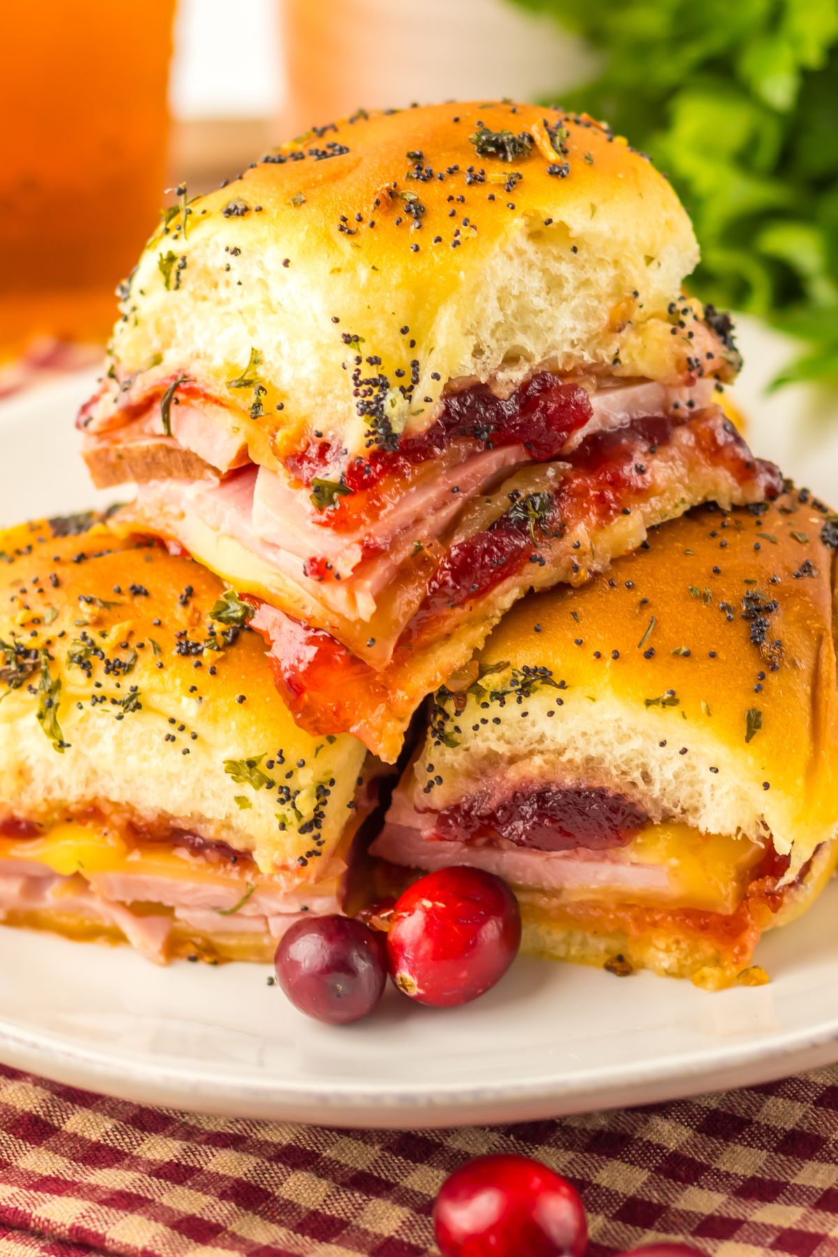 Cranberry and ham sliders stacked on a white plate with red cranberries as a garnish.