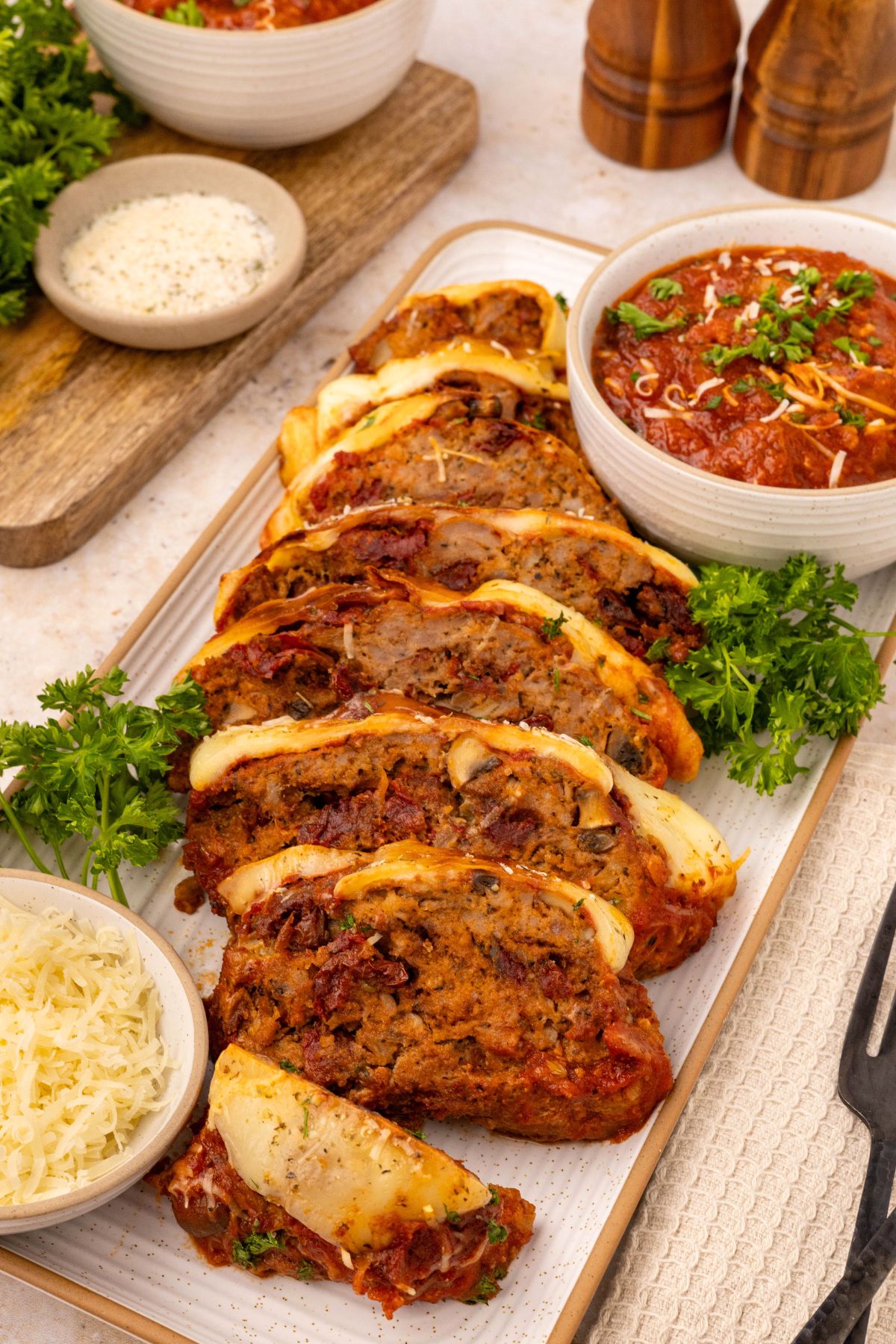 Slices of meatloaf on a rectangle serving dish with extra marinara sauce in a white dish. 