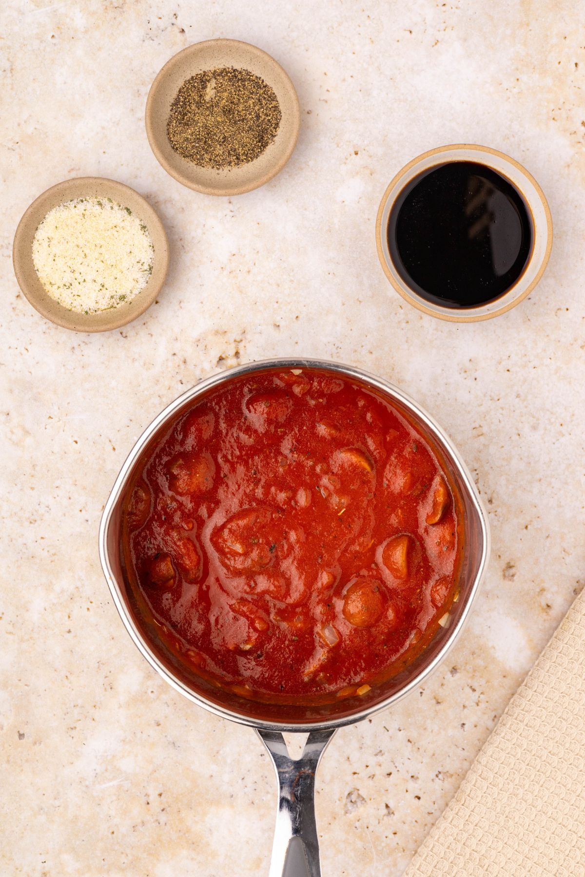 Ingredients needed for marinara sauce measured in dishes and a saucepan on a marble table. 