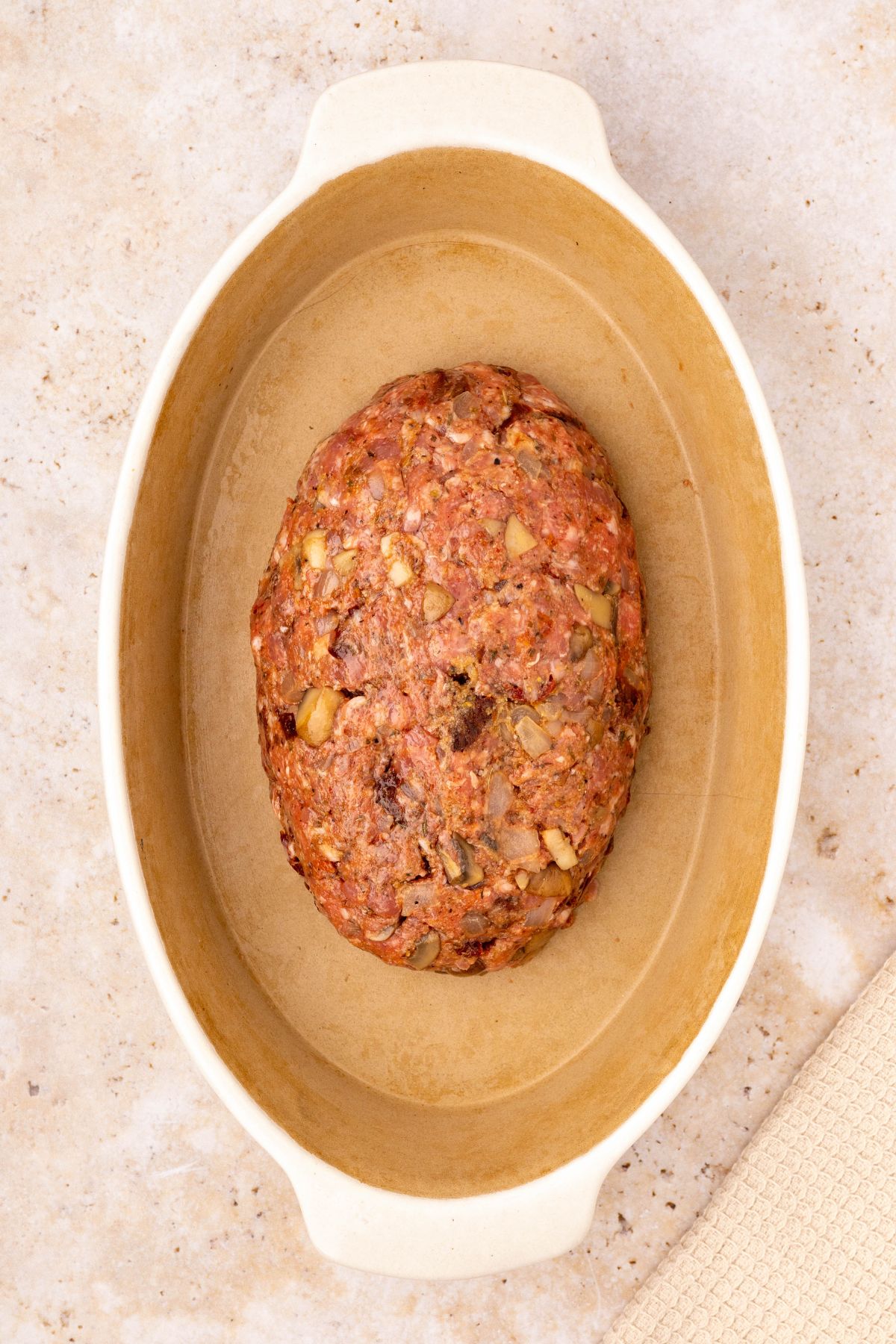 Uncooked meat shaped into a loaf, in an oval casserole dish. 