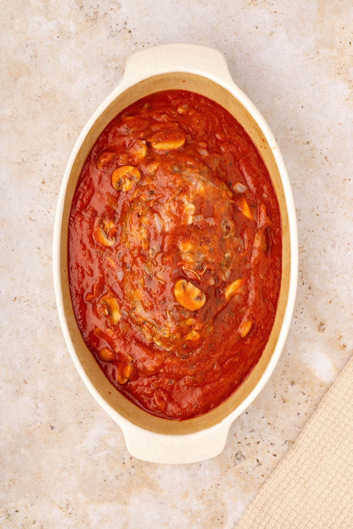 Meatloaf in a white casserole dish with marinara sauce over it, filling the dish. 