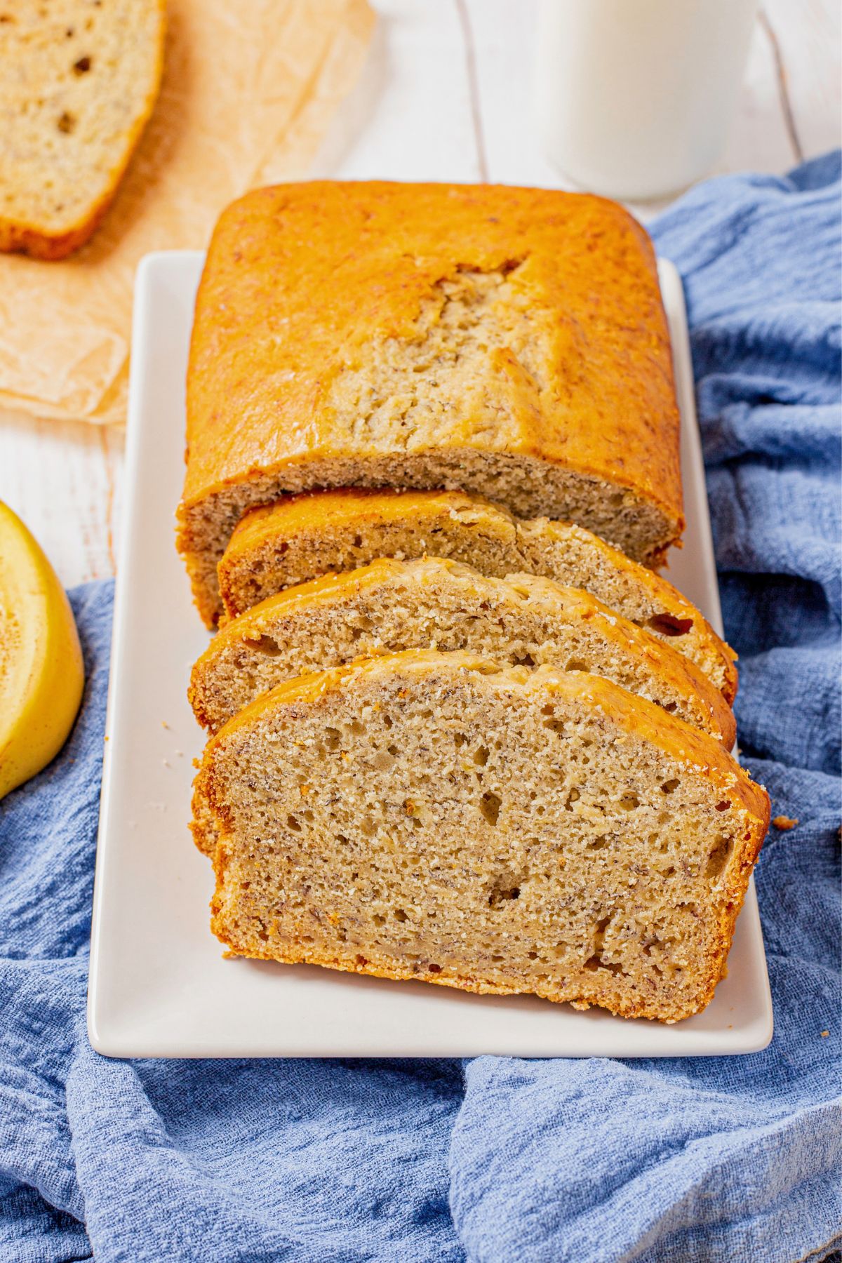 Moist banana bread on a white rectangle plate, cut into slices. 