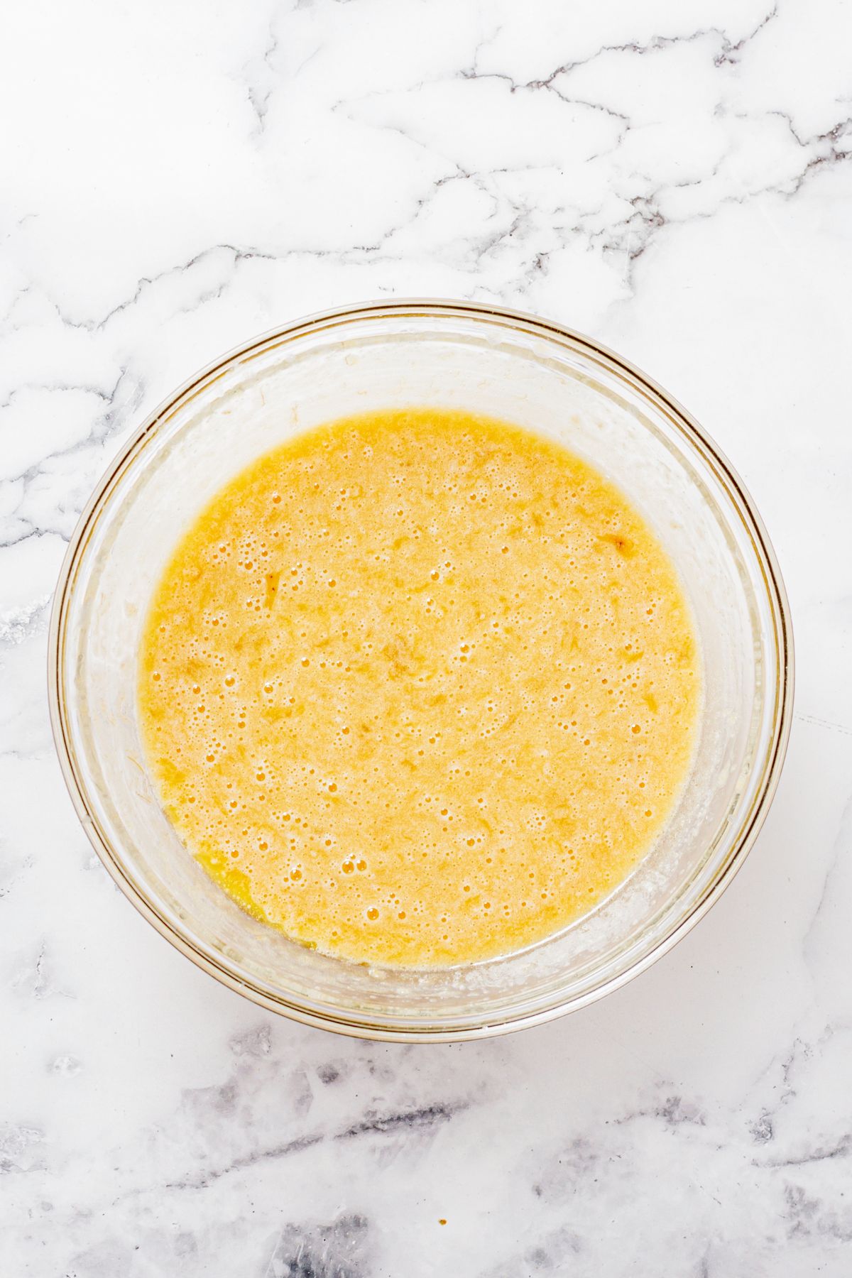 Mashed bananas with other ingredients in a large clear glass bowl. 