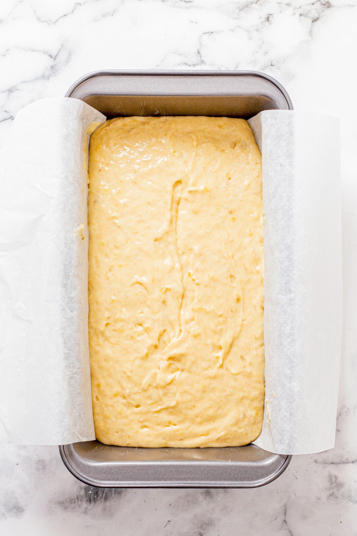 Uncooked bread batter in a metal loaf pan with parchment paper lining the pan. 