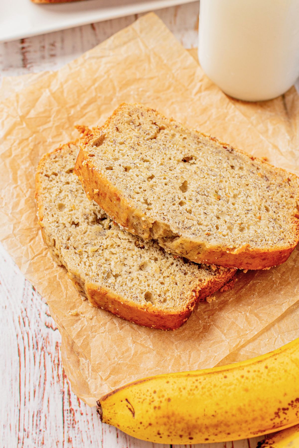 Slices of banana bread on a cutting board with a glass of milk and a banana. 