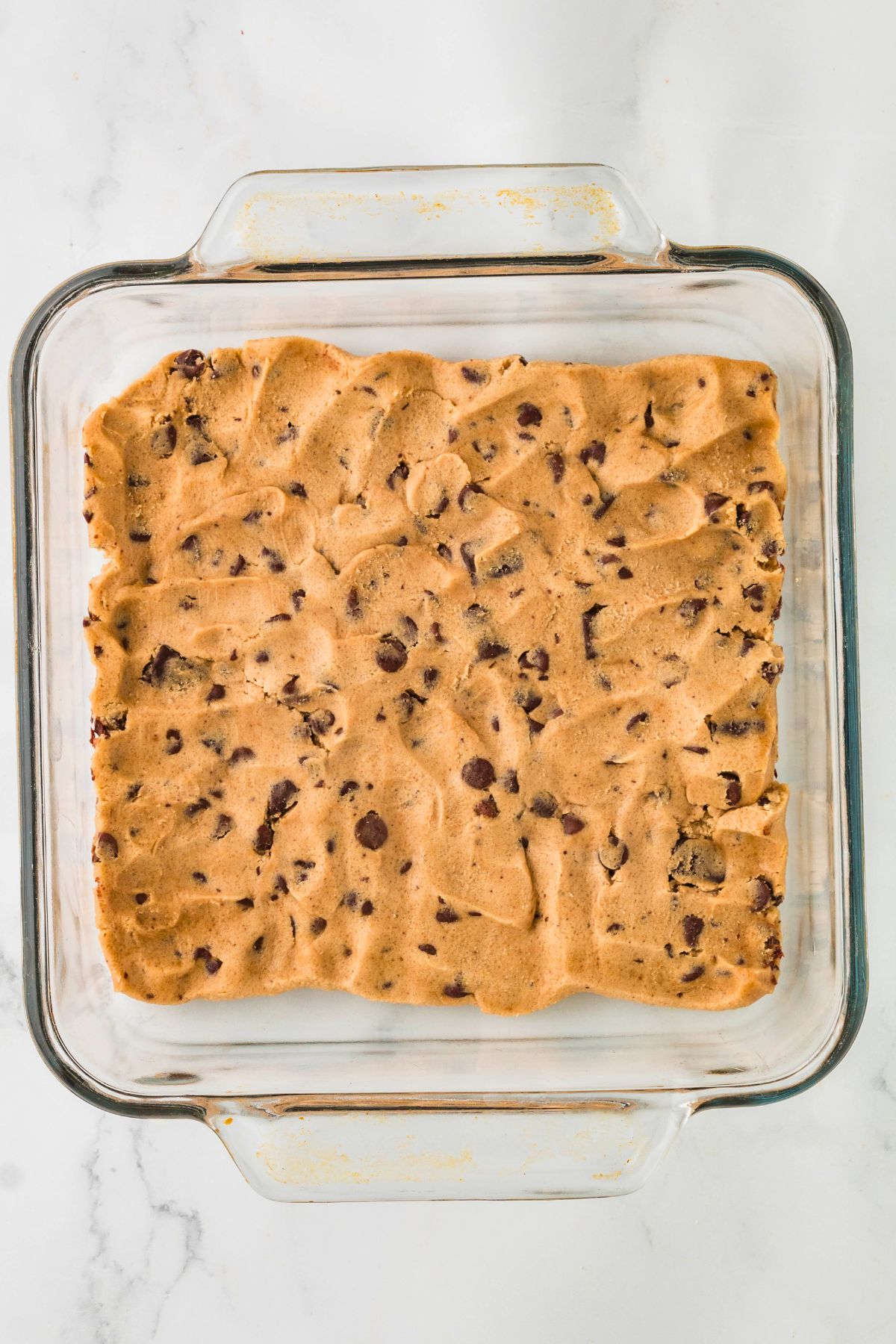 Uncooked chocolate chip cookie dough in a square baking dish.