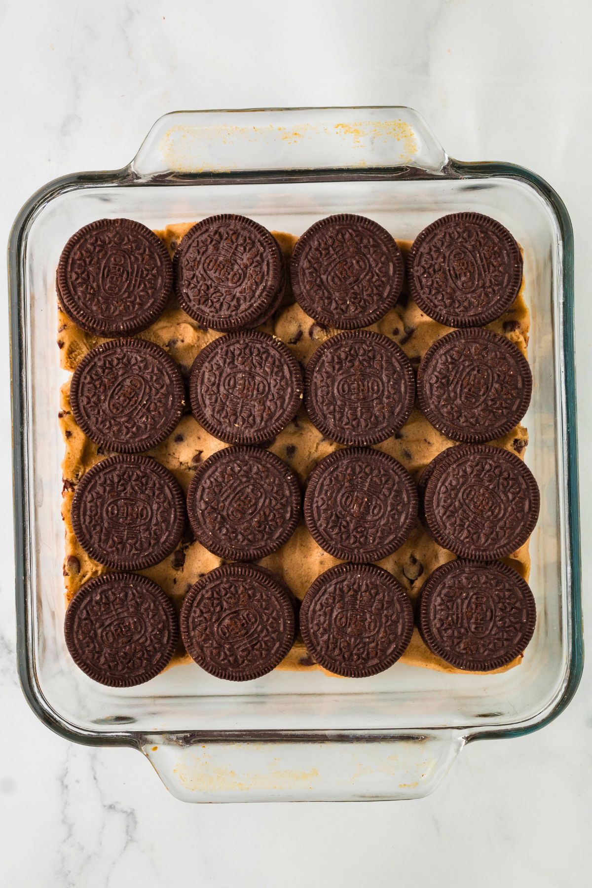 Oreo cookies topping uncooked chocolate chip cookie dough in a clear baking dish. 