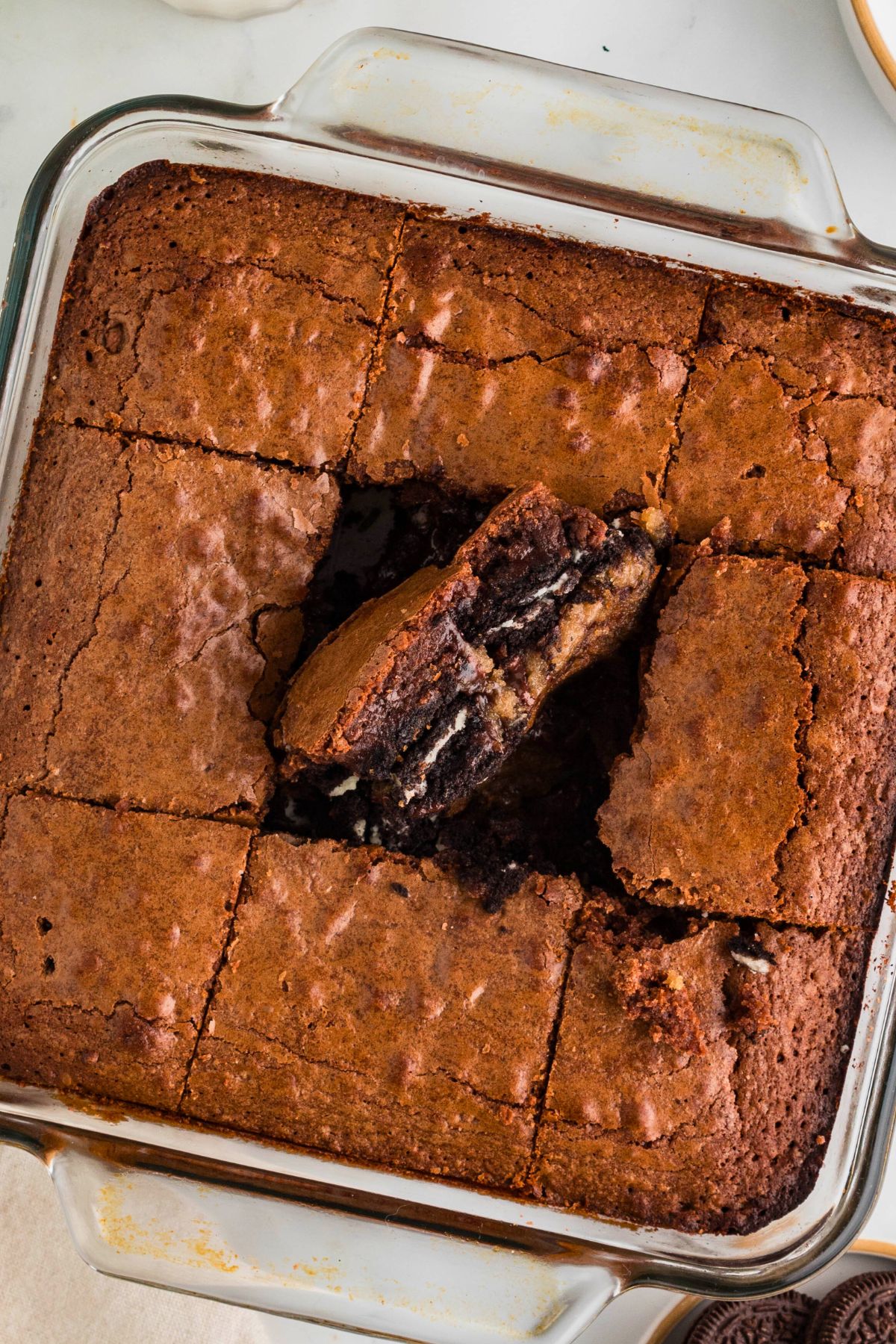 Brownies stuffed with Oreos over chocolate chip cookie dough baked and cut into squares in a clear baking dish. 