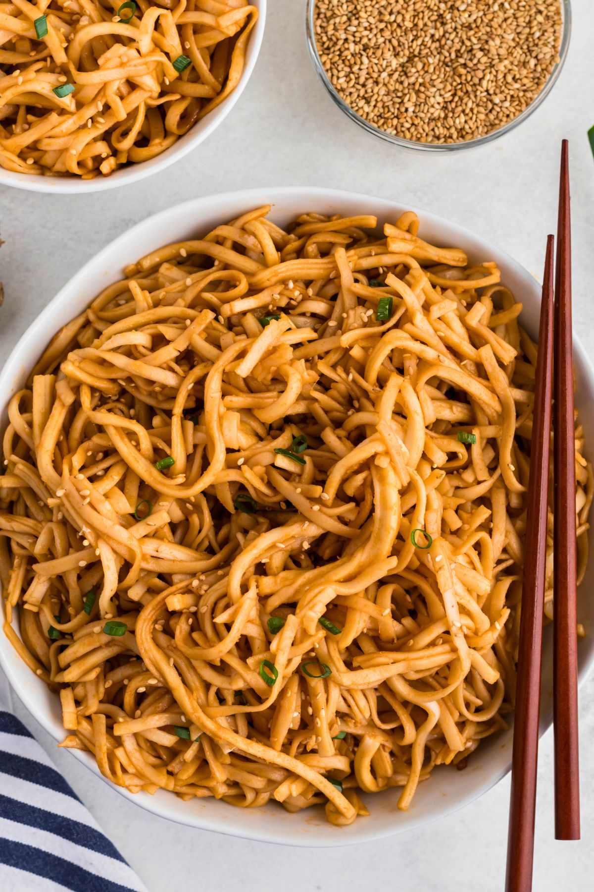 Spicy noodles tossed with sauce, served in a white bowl with chopsticks on the side of the bowl. 