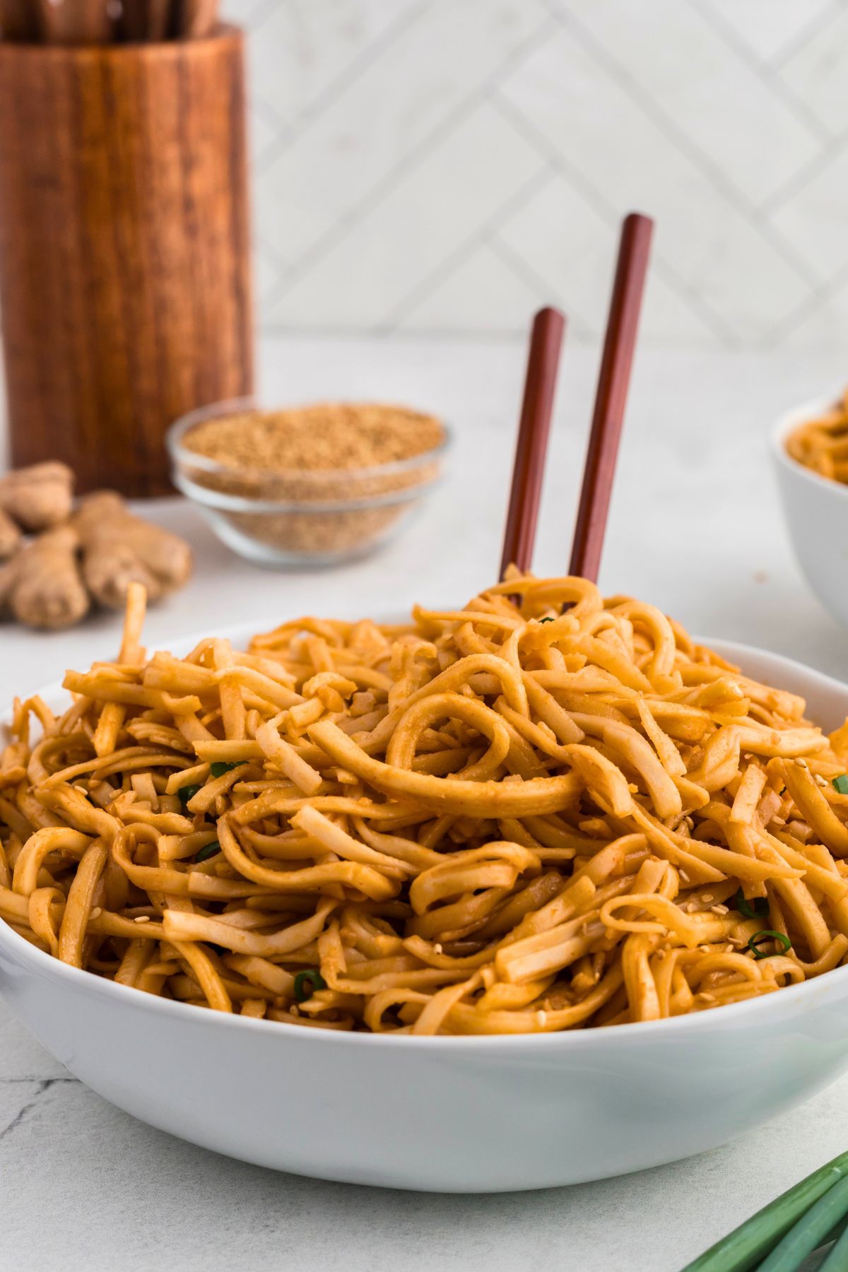 Spicy noodles served in a white bowl topped with chopsticks. 