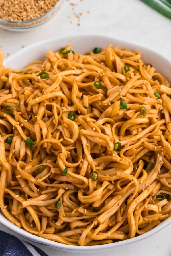 Spicy noodles tossed with sauce, served in a white bowl with chopsticks on the side of the bowl.